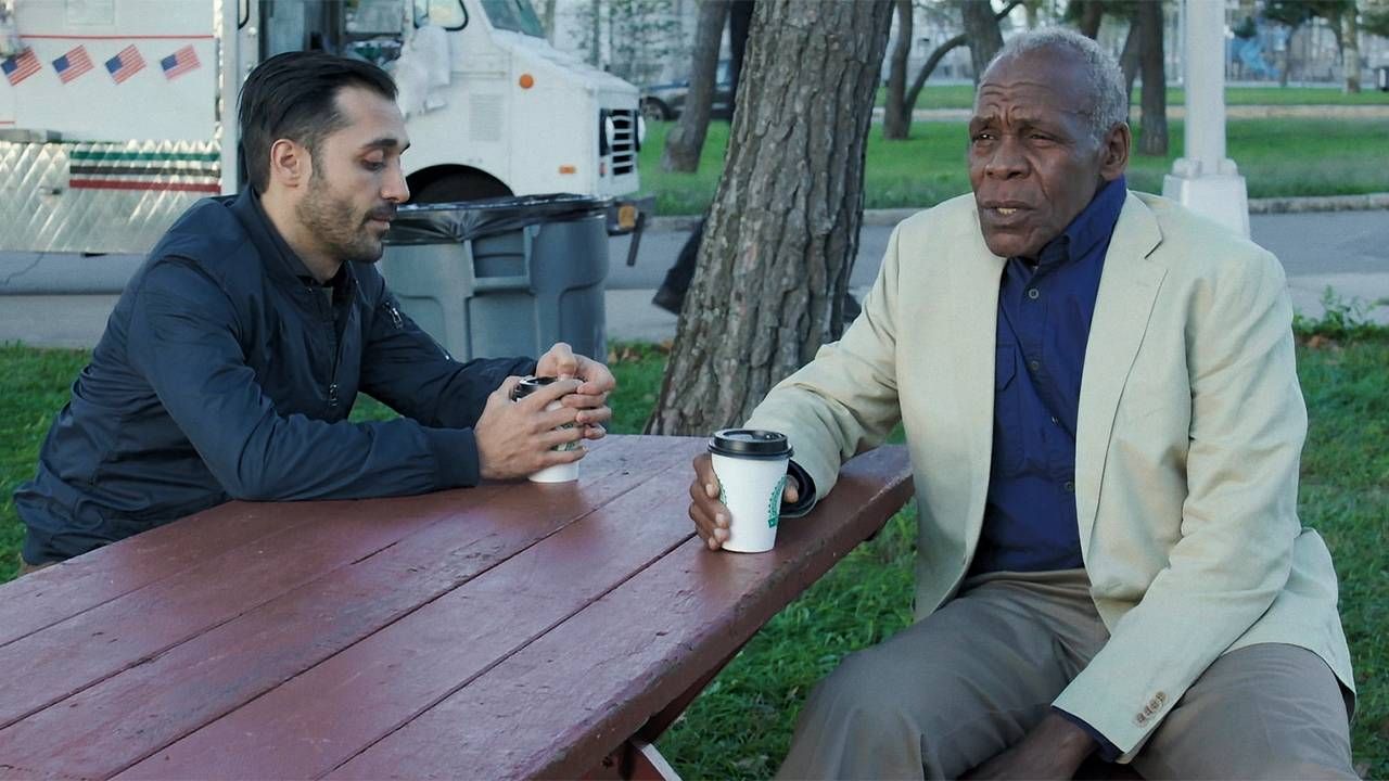 Danny Glover talking to someone at a picnic table in The Drummer. Next Avenue