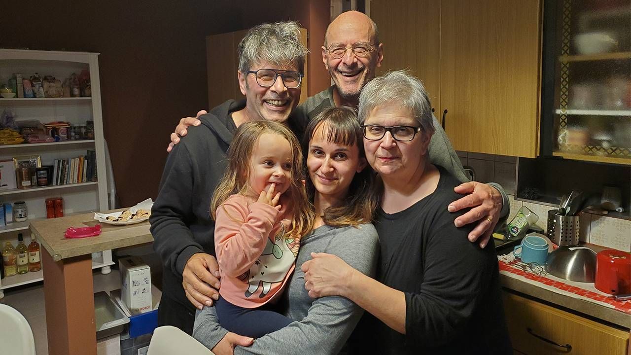 A small family hugging and smiling in a family kitchen. Next Avenue