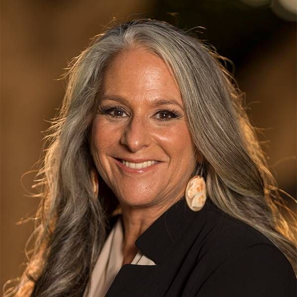 Headshot of a woman with long grey hair and colorful earrings. Next Avenue