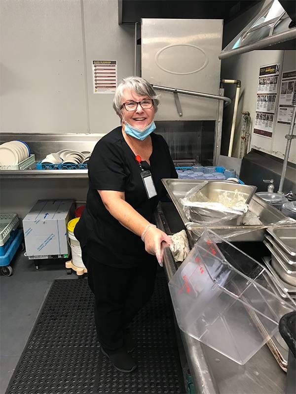 A person wearing a face mask and gloves standing in a dish pit doing dishes. Next Avenue