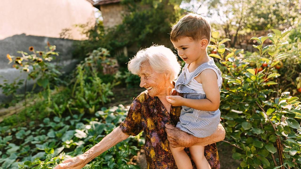 A woman in her old age holding a young grandchild showing him her garden, vitality, longevity, Next Avenue