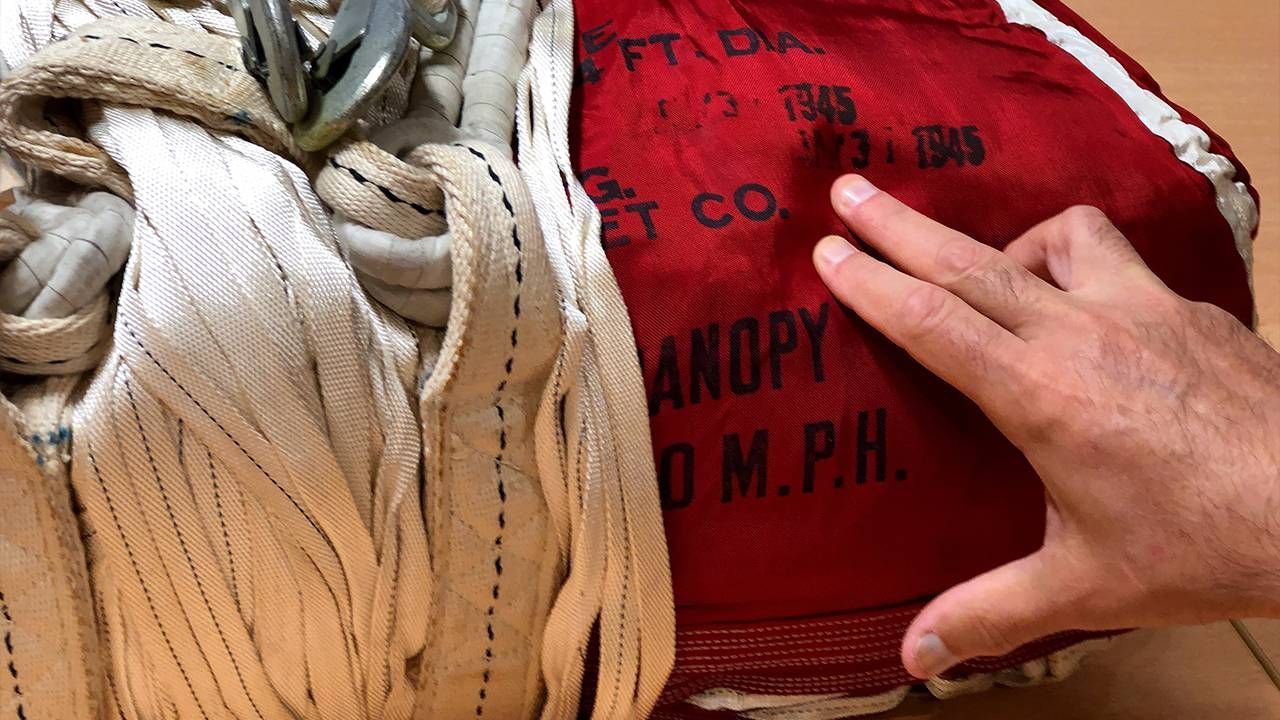 A person's hand pointing out the stamped lettering on the Normandy parachute. Next Avenue