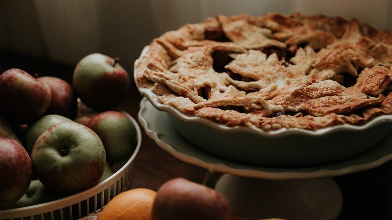 An apple pie sitting on a plate next to fresh apples for a small family thanksgiving gathering. Next Avenue