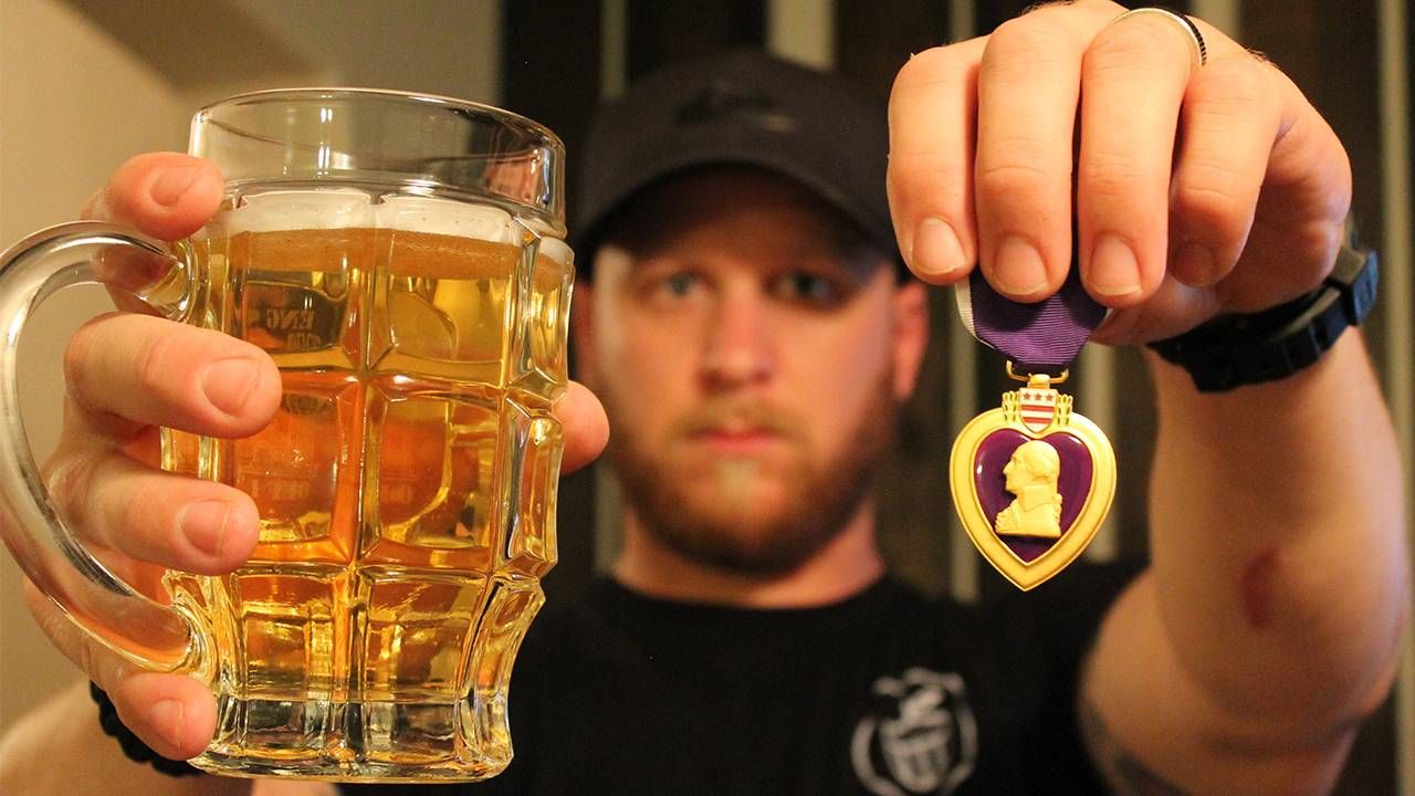 A veteran holding up a mug of cider in one hand and a purple heart medal in the other hand. Next Avenue, veterans, vets, craft cider