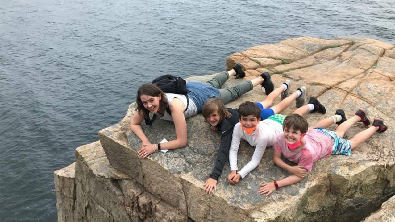 A parent and their 3 children laying on a rock overlooking water. Next Avenue, financial advice parents teens