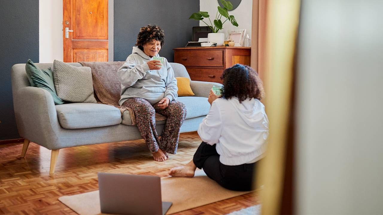 An older adult sitting on the couch with talking with adult daughter. Next Avenue, Parent's Sedentary Lifestyle