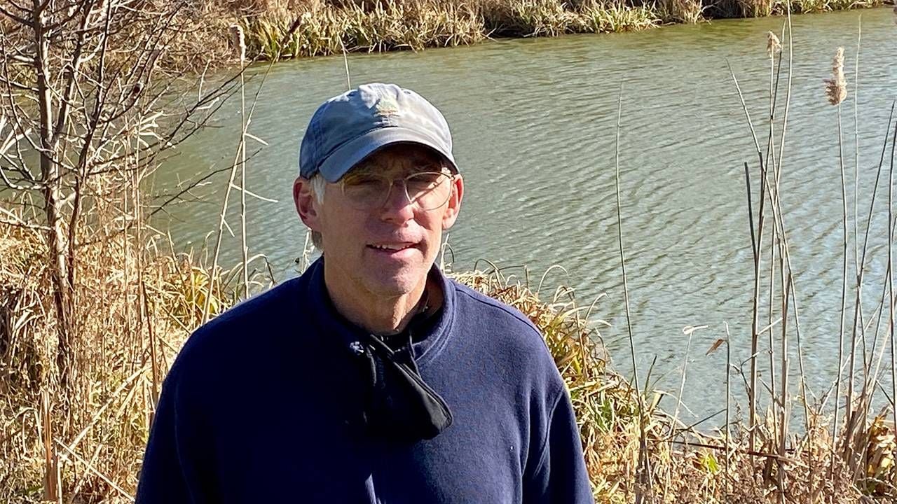 An older adult standing in front of a pond outside. Next Avenue, what to do in retirement