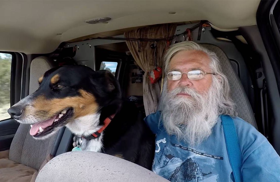 A man with grey hair sitting next to his dog in the driver's seat of an RV. Next Avenue, RV living, Nomadland, Bob Wells