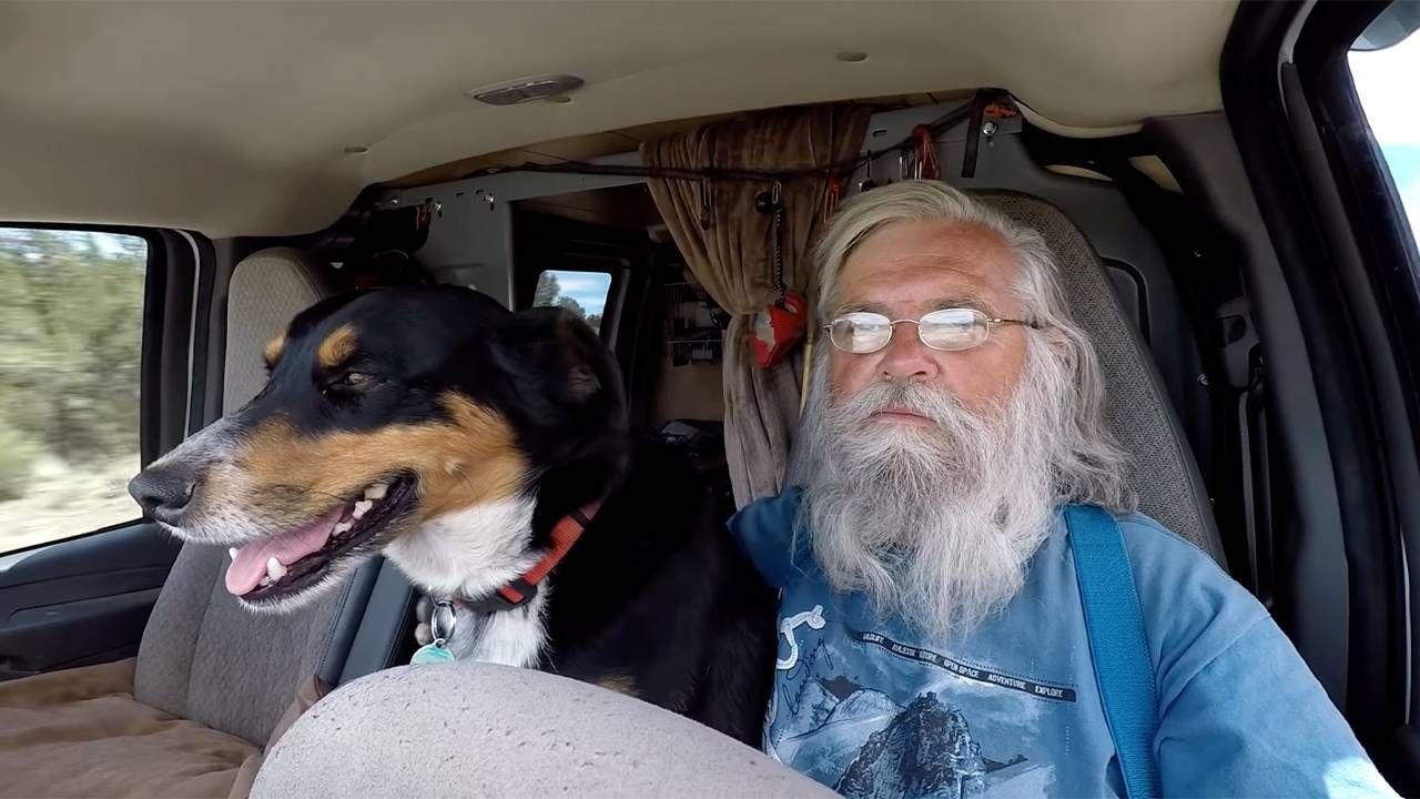 A man with grey hair sitting next to his dog in the driver's seat of an RV. Next Avenue, RV living, Nomadland, Bob Wells