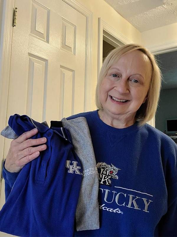 A woman holding up sweatshirts and smiling at home. Next Avenue, buy nothing project