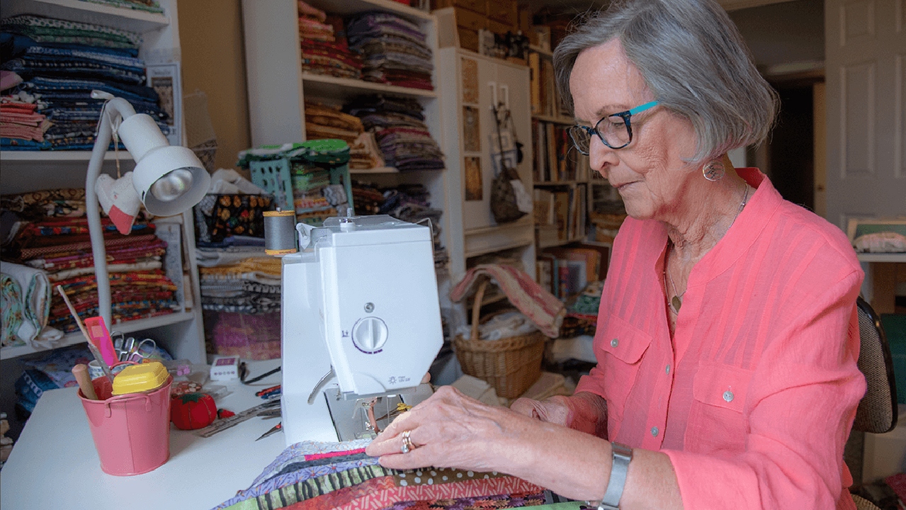 A woman sitting down to sew in a sewing room. Next Avenue