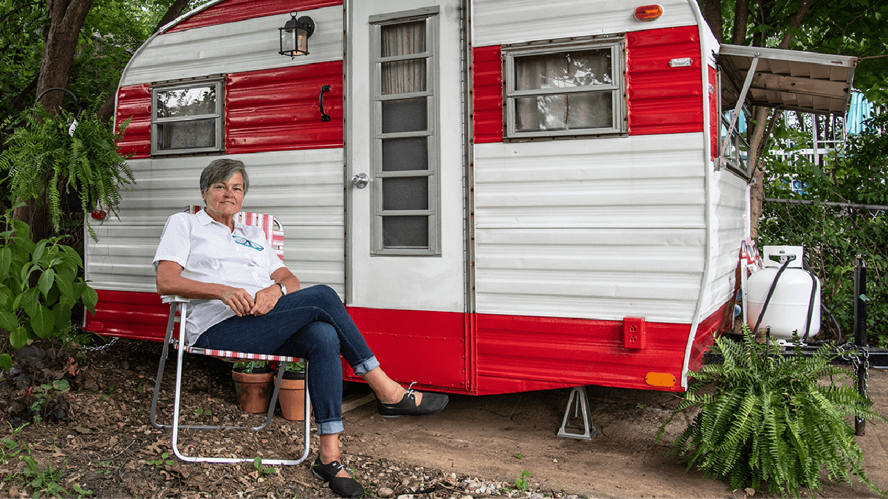 A woman sitting in front of a small red and white camping RV. Next Avenue