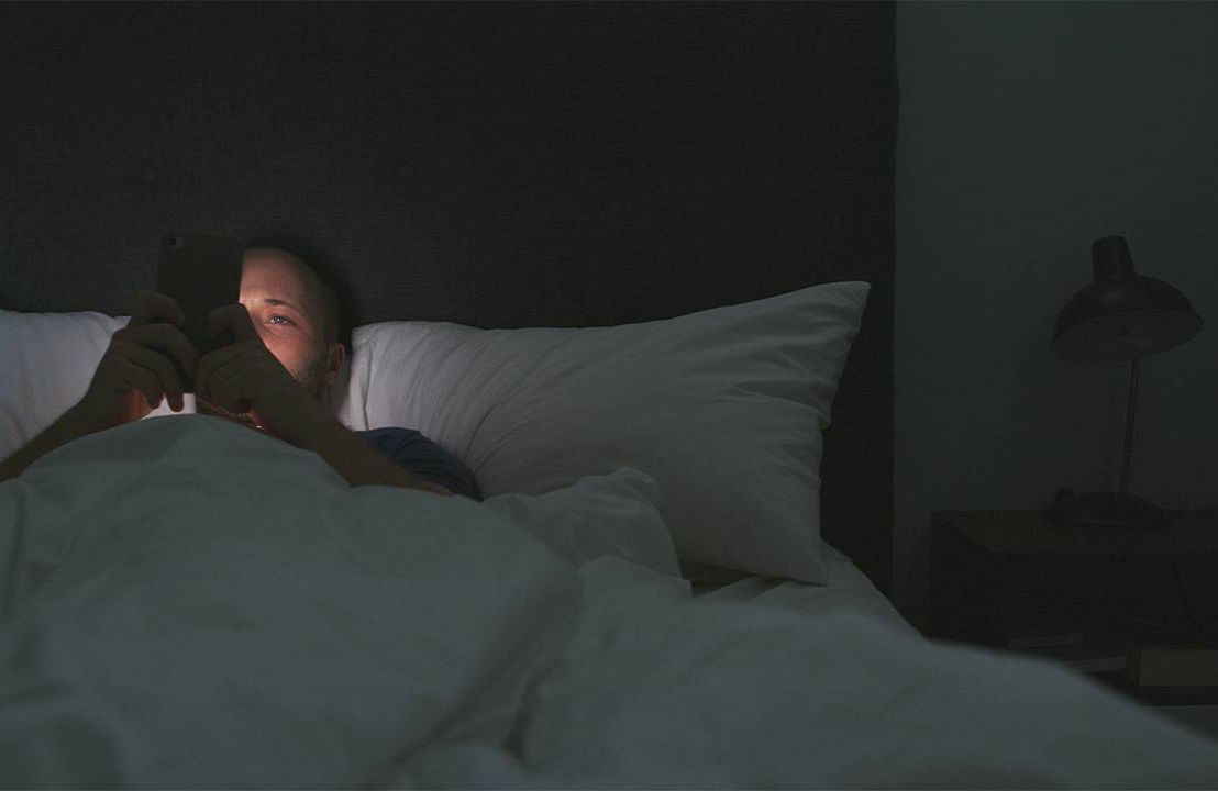 A person lying in bed at night awake, lit up by the light of their cell phone. Next Avenue, Insomnia,