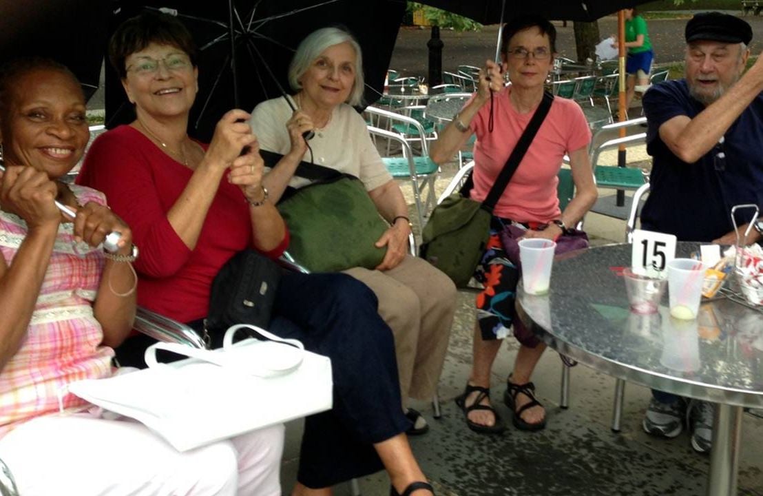 A group of people sitting outside at a restaurant holding umbrellas. Next Avenue, learning about aging