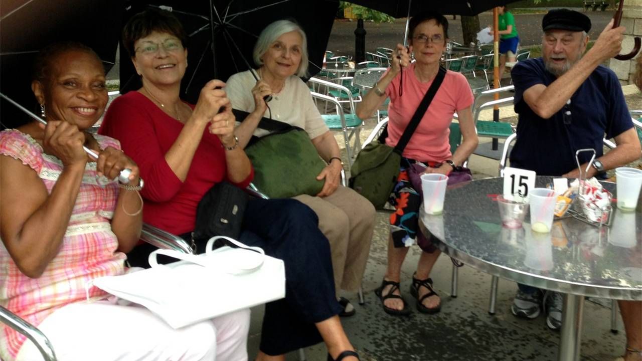 A group of people sitting outside at a restaurant holding umbrellas. Next Avenue, learning about aging