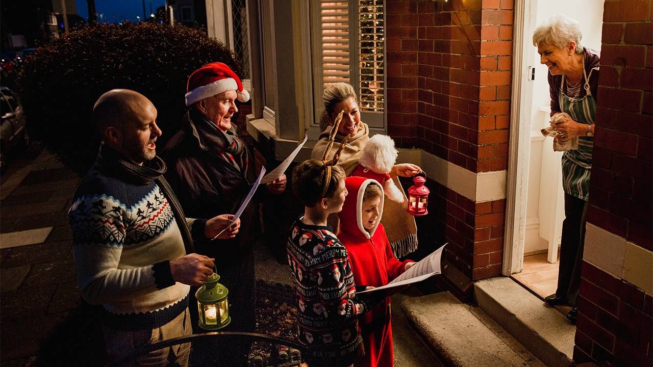 A group of older and younger people caroling at someone's doorstep. Next Avenue make room at the table, loneliness isolation