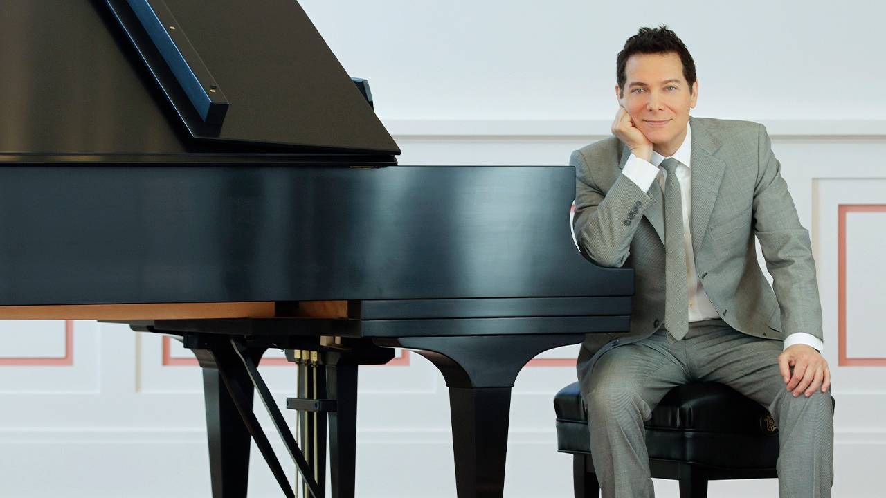 A man with dark hair sitting at a piano bench. Next Avenue, The great American Songbook, Michael Feinstein