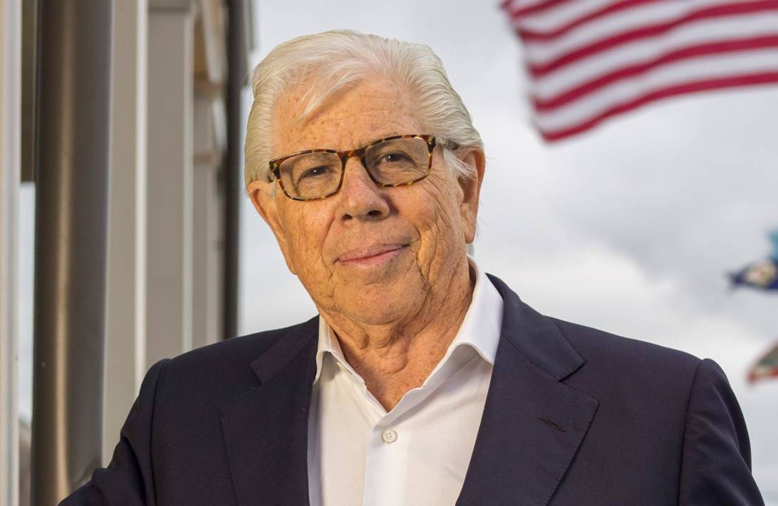 A recent photo of Carl Bernstein standing outside in front of a flag. Next Avenue