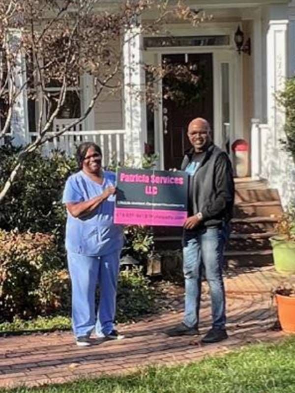 A woman and a man holding up a sign in a front yard. Next Avenue, lifestyle assistant, entrepreneur, small business, marketing strategy
