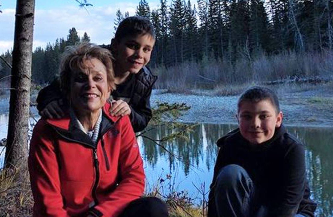 A grandmother kneeling with her two grandsons near a creek. Next Avenue