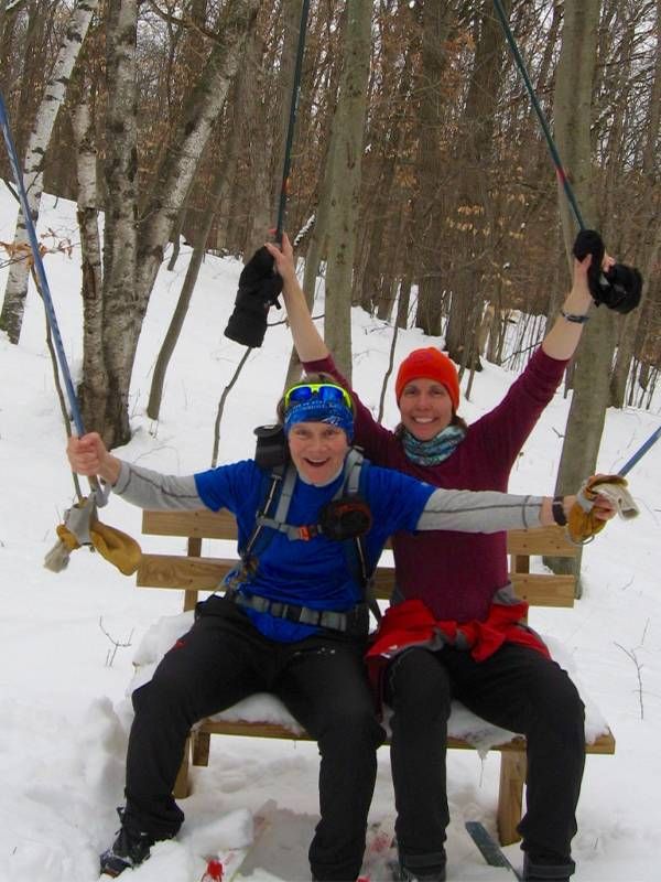 Two older adults sitting on a bench in the snow, smiling and holding up their ski poles. Next Avenue, Skiing safely middle age