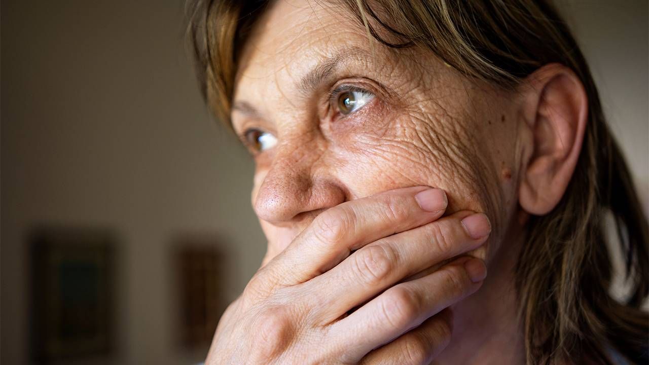 An older adult having a panic attack and covering her mouth with her hand. Next Avenue