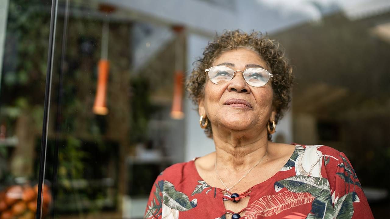 A woman with curly hair looking out a window. Next Avenue, Medicare, Medicaid, Alzheimer's, Aduhelm