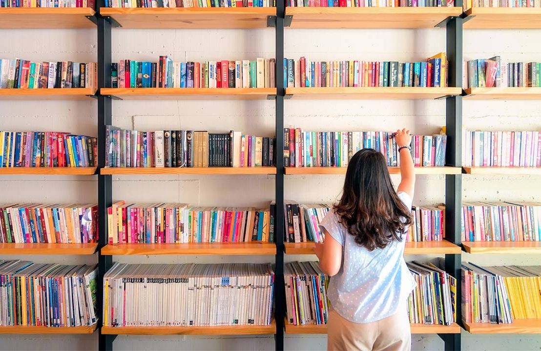A woman standing in front of a shelf filled with picture books. Next Avenue