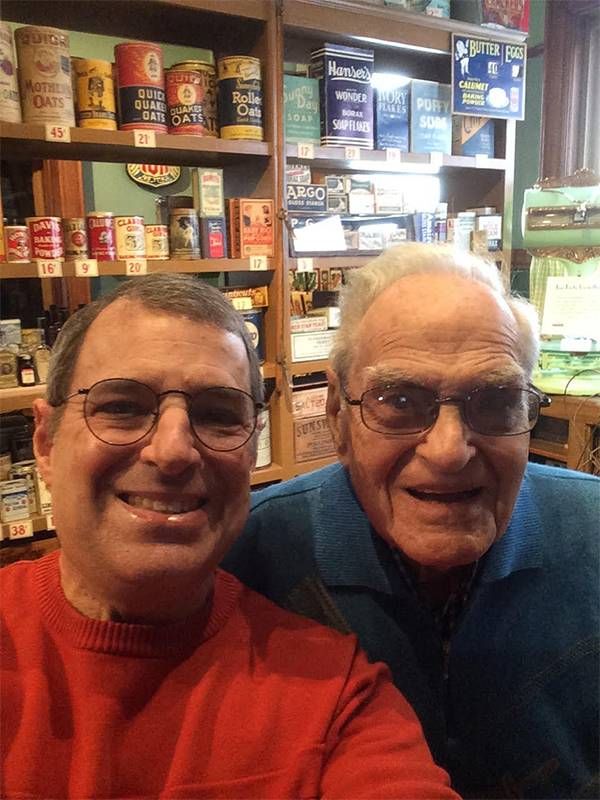Two older adults wearing glasses and smiling in front of vintage items. Next Avenue