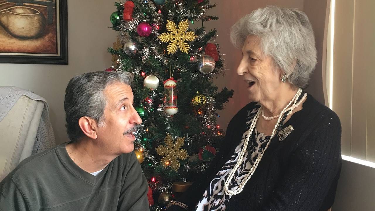 An adult son looking up at his older mother in front of a christmas tree. Next Avenue, palliative care, caregiving