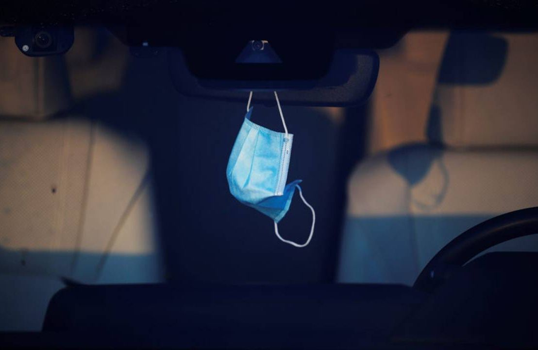 A face mask hanging from a person's car rear view mirror. Next Avenue, long covid, long haul covid