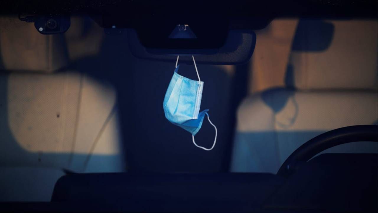 A face mask hanging from a person's car rear view mirror. Next Avenue, long covid, long haul covid