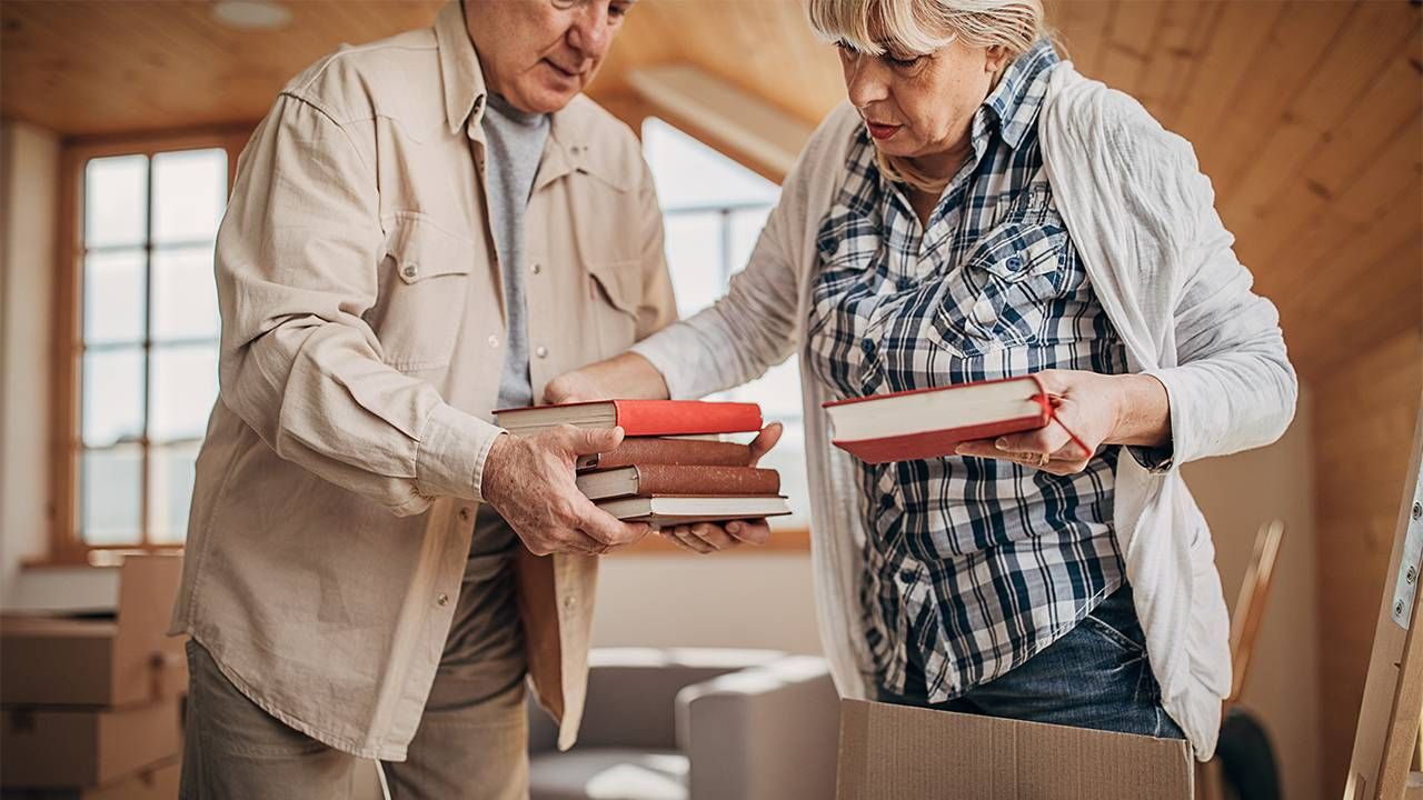 A couple sorting through old books in a box. Next Avenue, downsizing, decluttering, relationship conflict