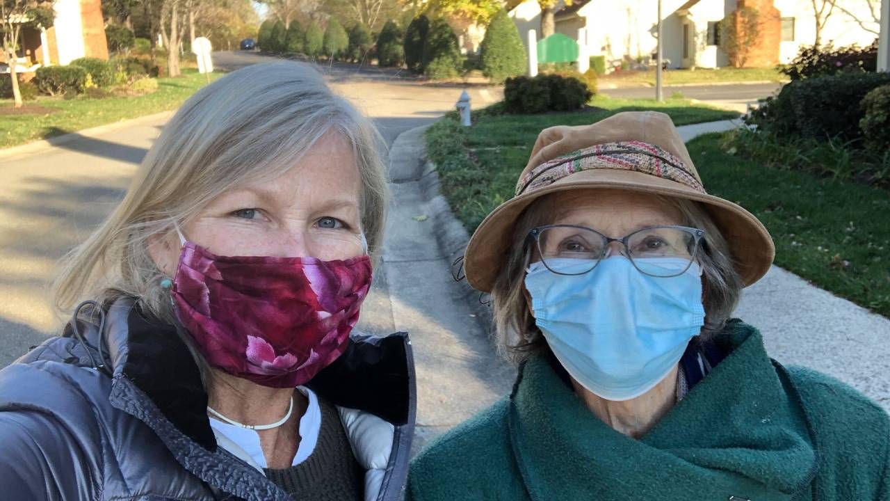 Two older adults wearing face masks walking outside after connecting through Naborforce. Next Avenue
