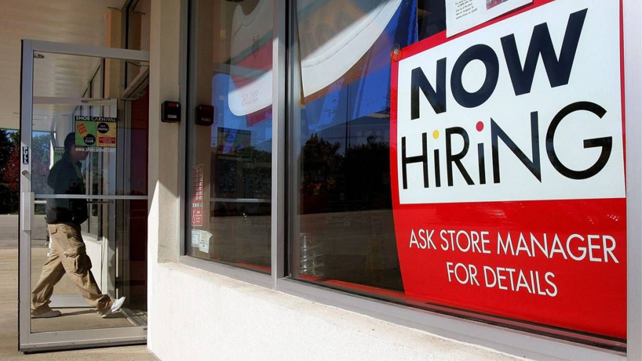 An older adult entering a store with a now hiring sign in the window. Next Avenue, job market 2022