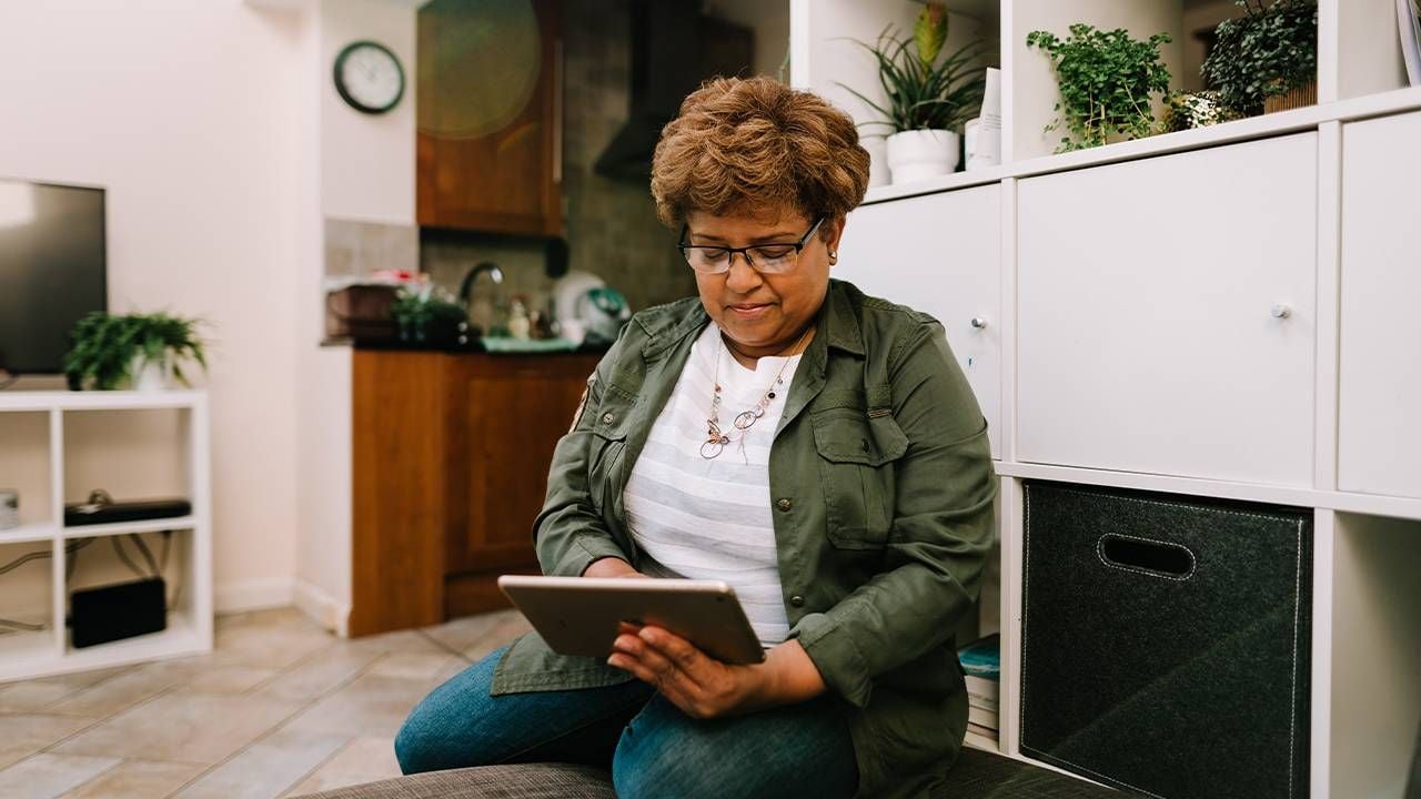 An older adult sitting on a couch looking at a mobile finance app on her ipad. Next Avenue