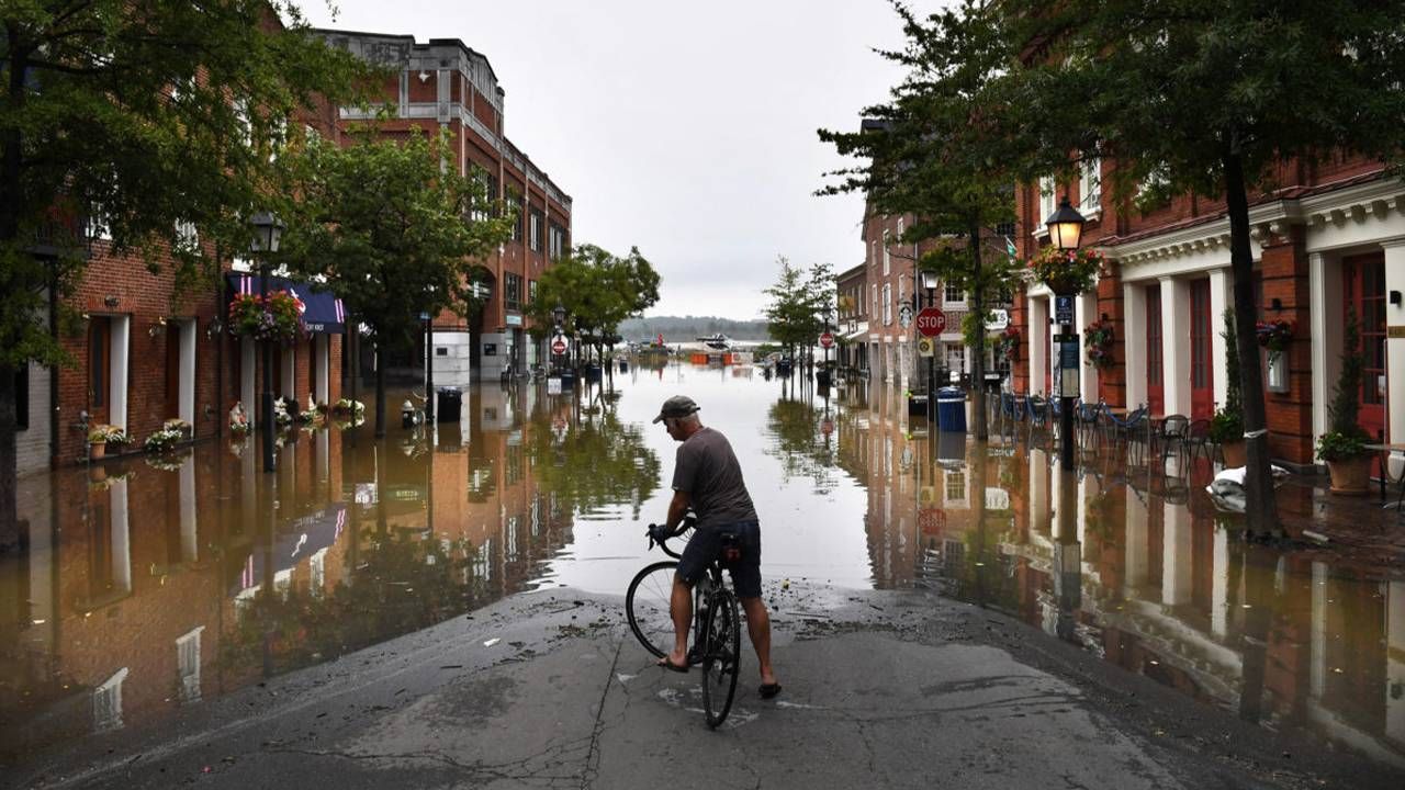 An older adult on a bicycle in the street has come to a stop and blocked by flood water. Next Avenue, climate change, report, the new climate war