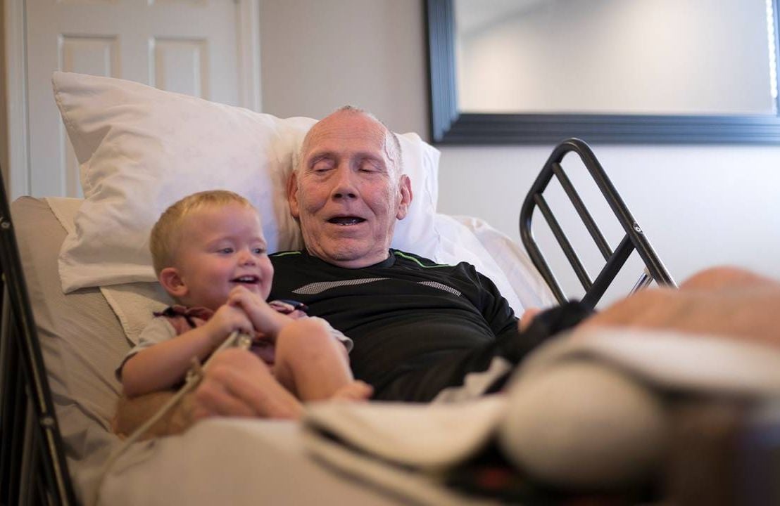 An older palliative care patient sitting in a bed with his grandson. Next Avenue