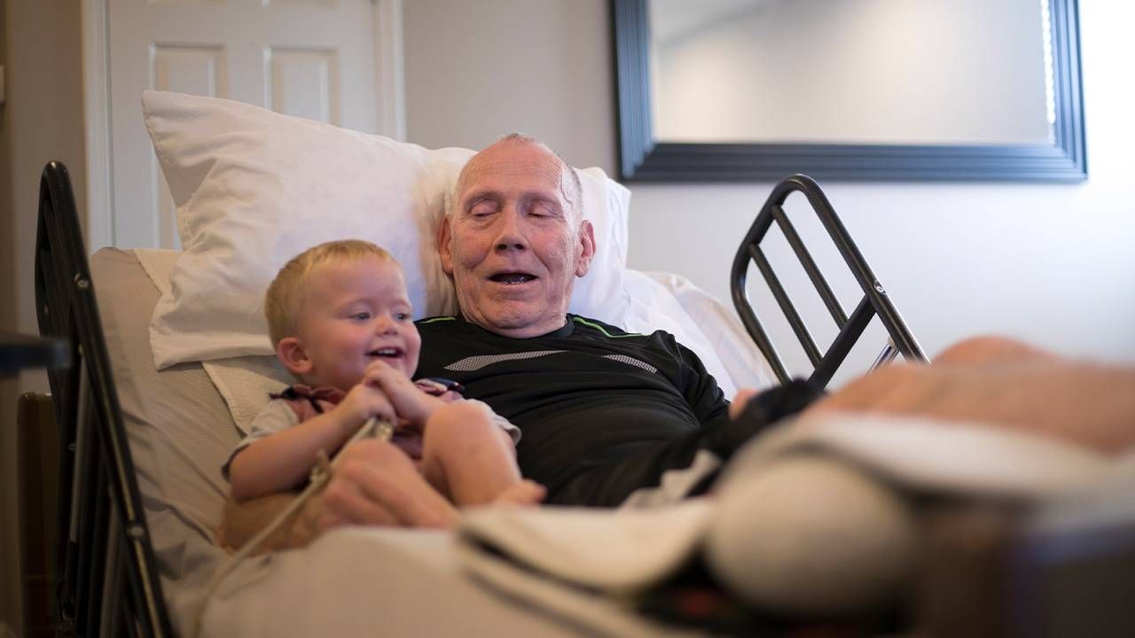 An older palliative care patient sitting in a bed with his grandson. Next Avenue