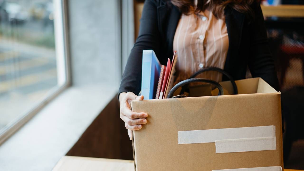 A person holding a box of items from their desk after being laid off from work. Next Avenue