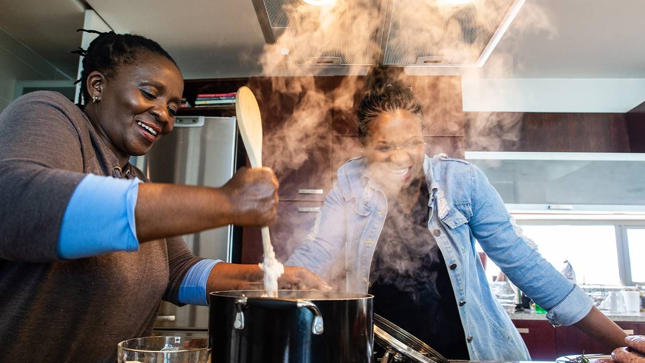 An older adult cooking in the kitchen with her adult child caregiver. Next Avenue, setting boundaries, privacy caregiving