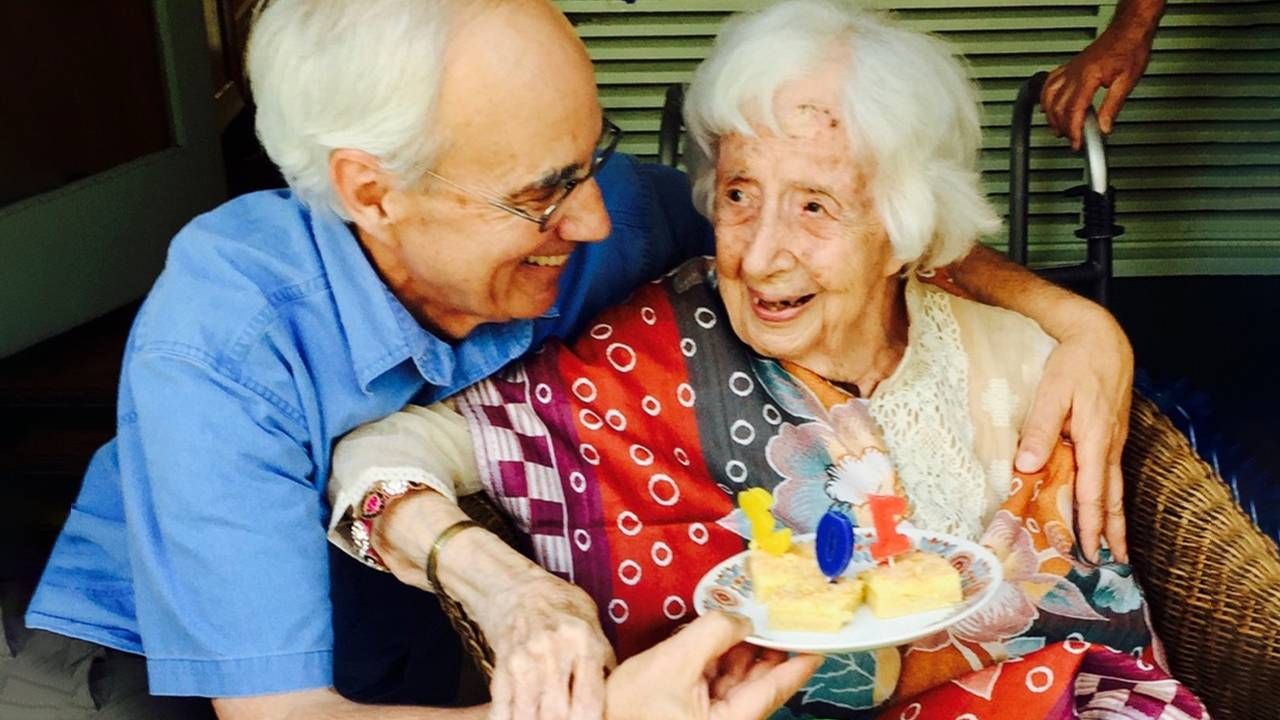 An older caregiver presenting his aging mother with a birthday cake. Nect Avenue, caregiving advice, caregiving for a parent