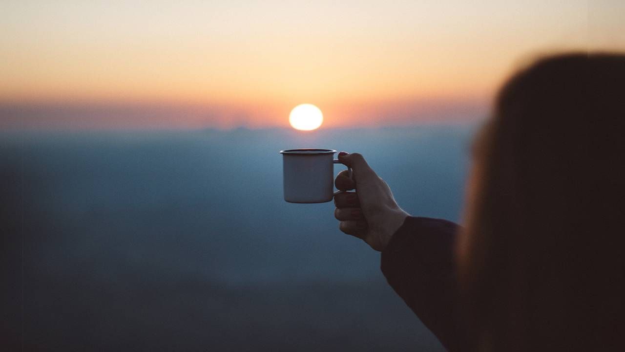 A person holding up a mug of coffee as the sun rises in the background. Next Avenue, coffee good for you, health