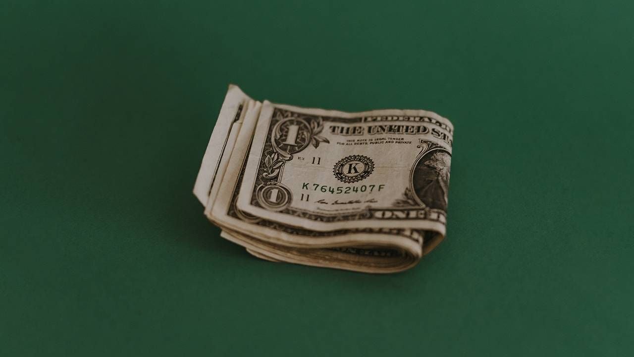 A few folded up one dollar bills on a dark green background. Next Avenue, financial anxiety, worried about money
