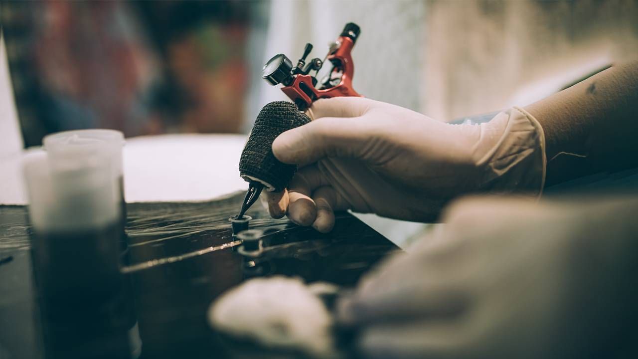 A tattoo artist holding a tattoo gun and putting ink on the tip. Next Avenue, first tattoo, tattoos older adults