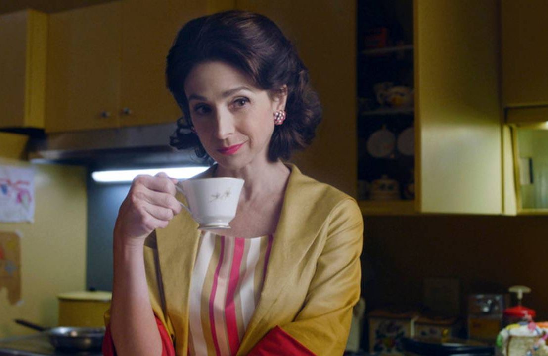 A 1950s styled kitchen with a woman holding a teacup. Next Avenue, The Marvelous Mrs. Maisel, Marin Hinkle