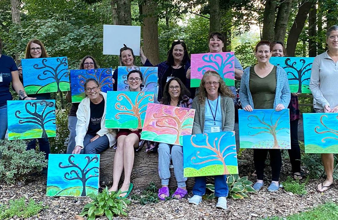 A group of people holding up paintings while standing in a forest. Next Avenue, dna, family tree discoveries