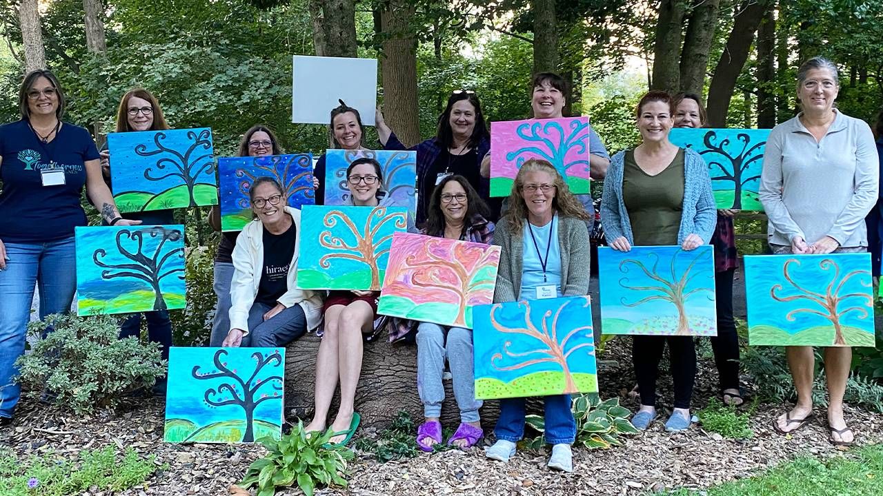 A group of people holding up paintings while standing in a forest. Next Avenue, dna, family tree discoveries