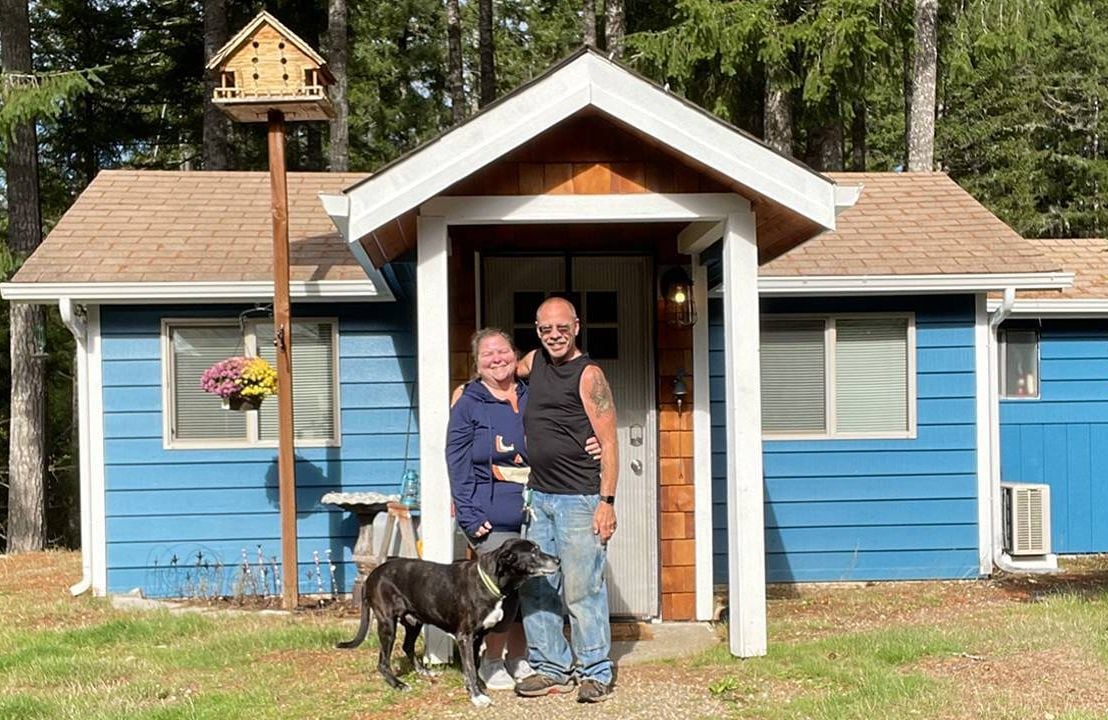 An older couple standing with their dog outside of their tiny house. Next Avenue, tiny house movement