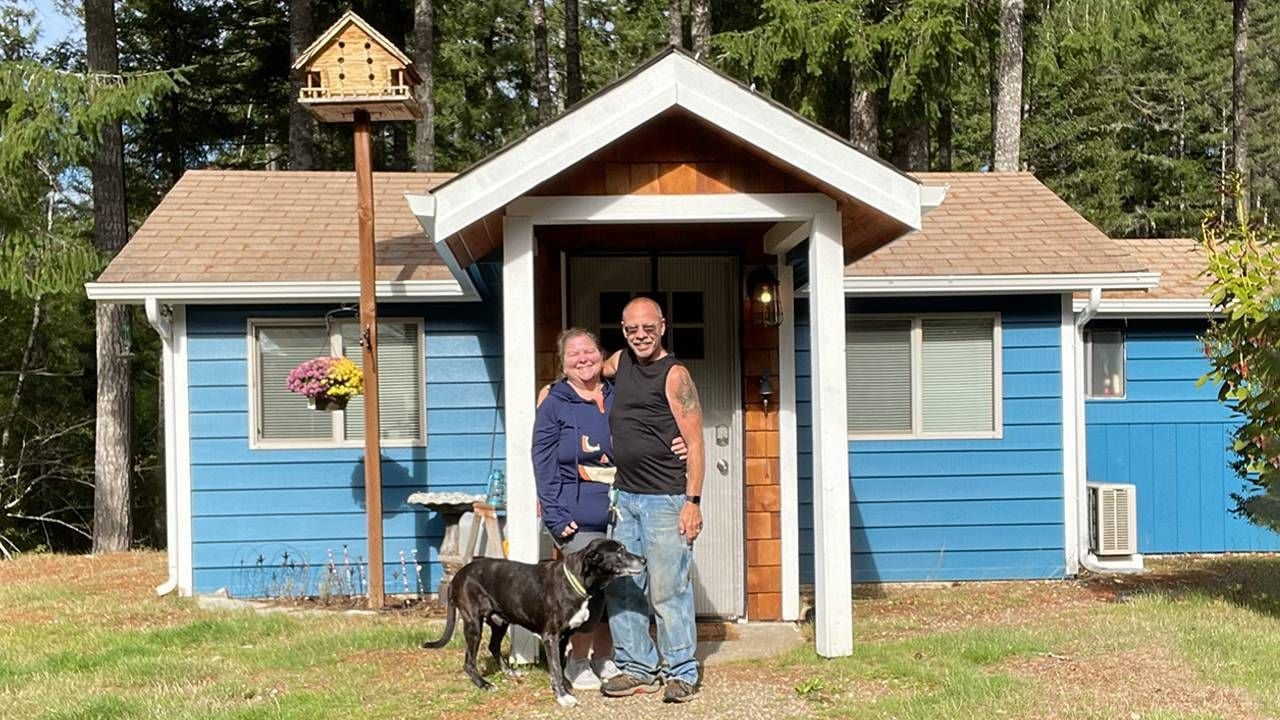 An older couple standing with their dog outside of their tiny house. Next Avenue, tiny house movement